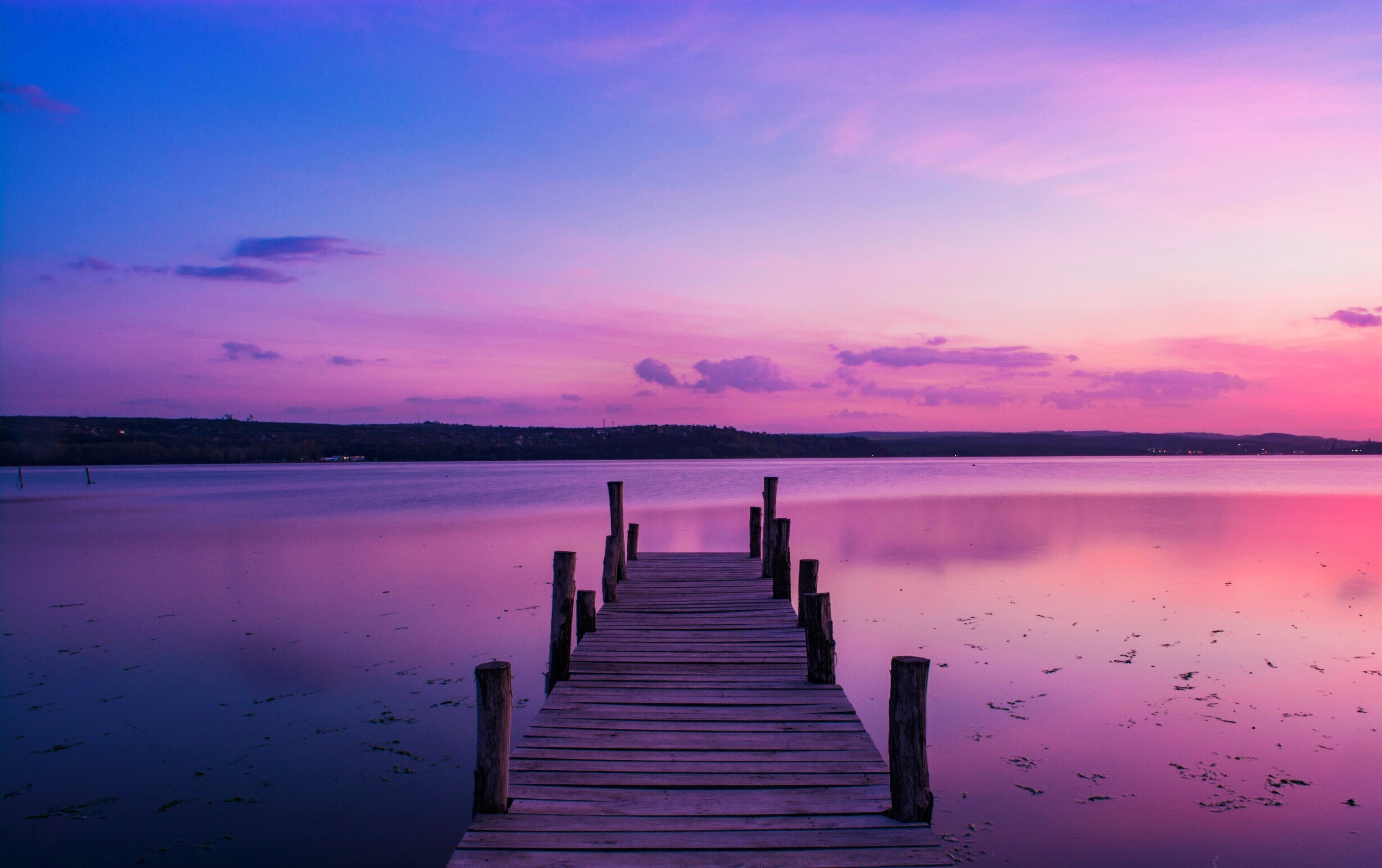 A wooden pier extending into calm water with a colorful sunset sky.
