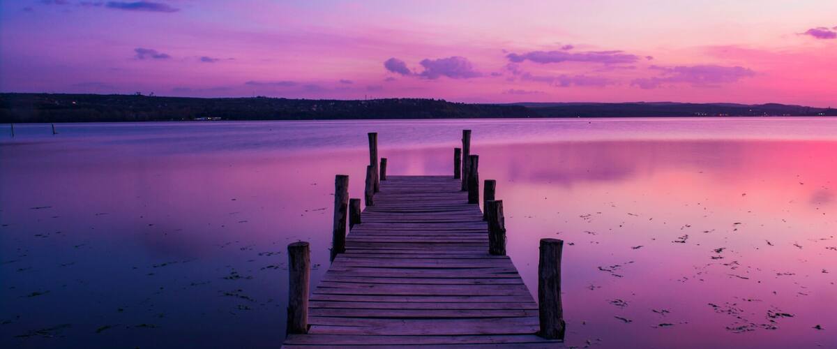 A wooden pier extending into calm water with a colorful sunset sky.