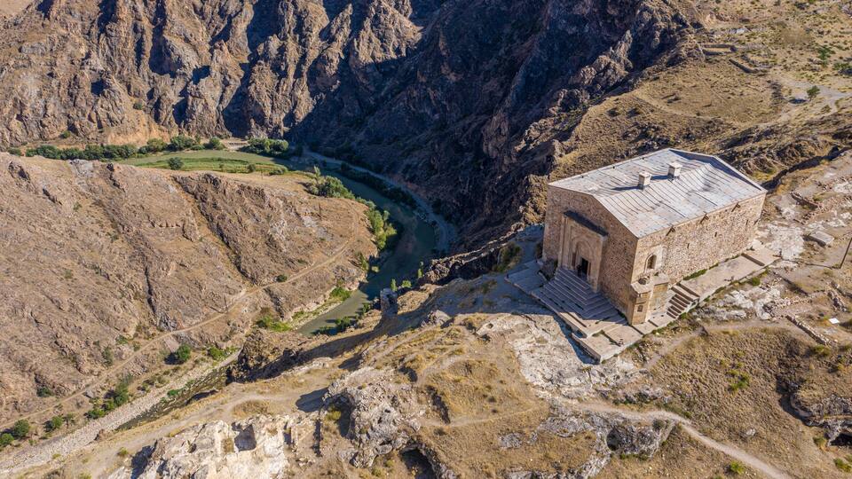 A stone building with a flat roof near a river in a canyon.