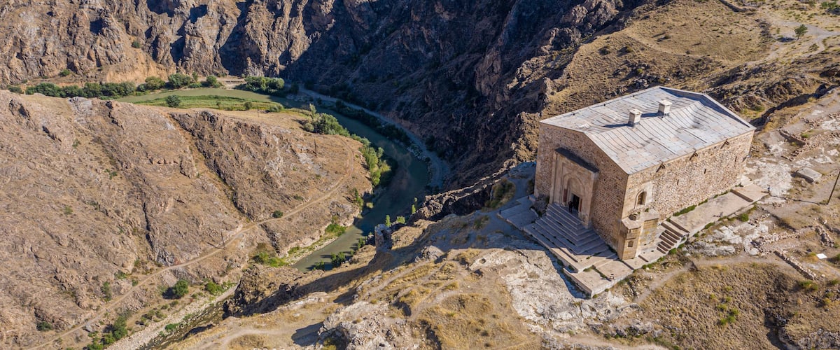A stone building with a flat roof near a river in a canyon.