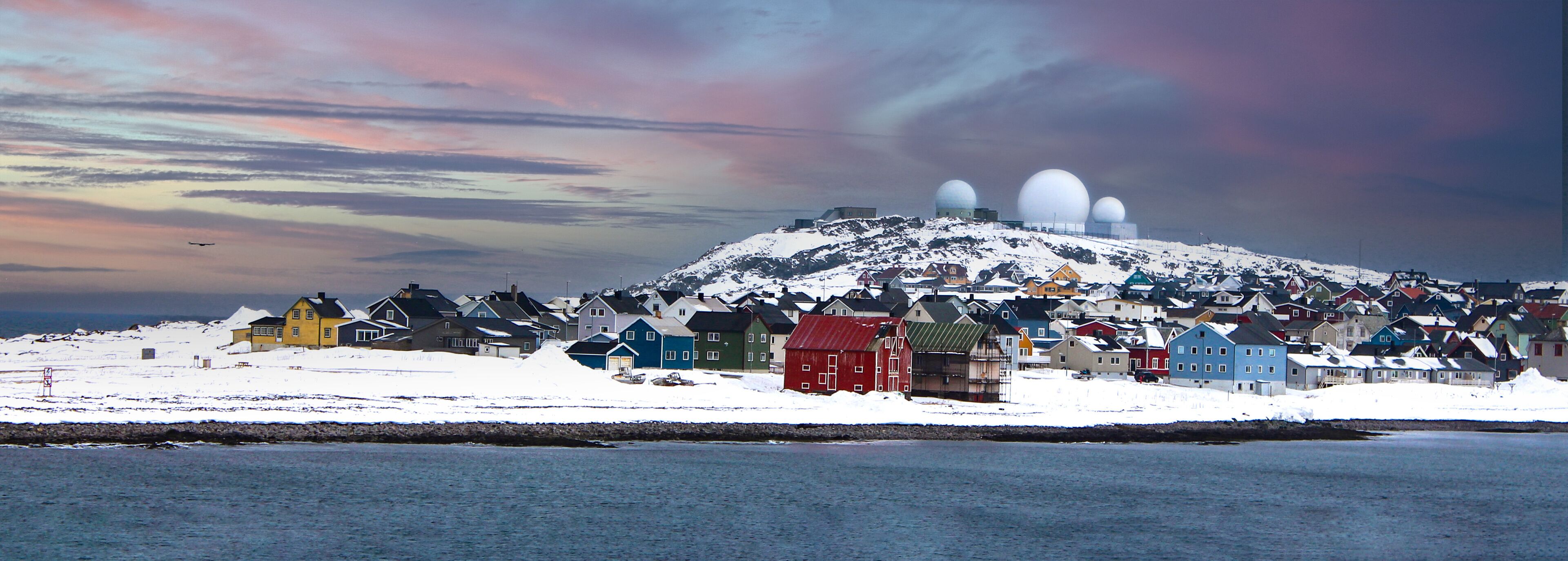 A snowy landscape with a cluster of colorful houses and a large dome structure on a hill.