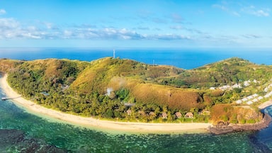 An aerial view of a tropical island with a crescent-shaped coastline, clear turquoise waters, and lush greenery.