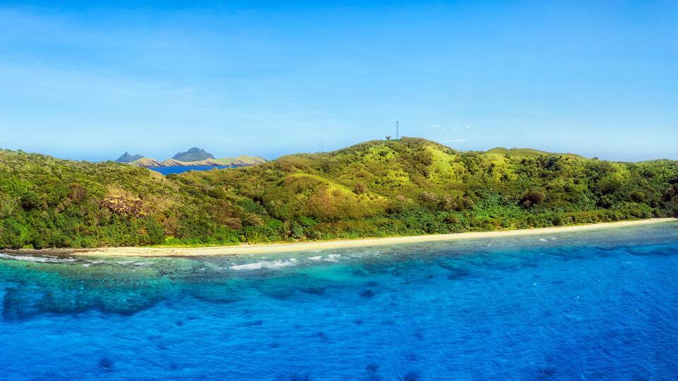 A tropical island with a sandy beach and lush greenery surrounded by clear blue waters.
