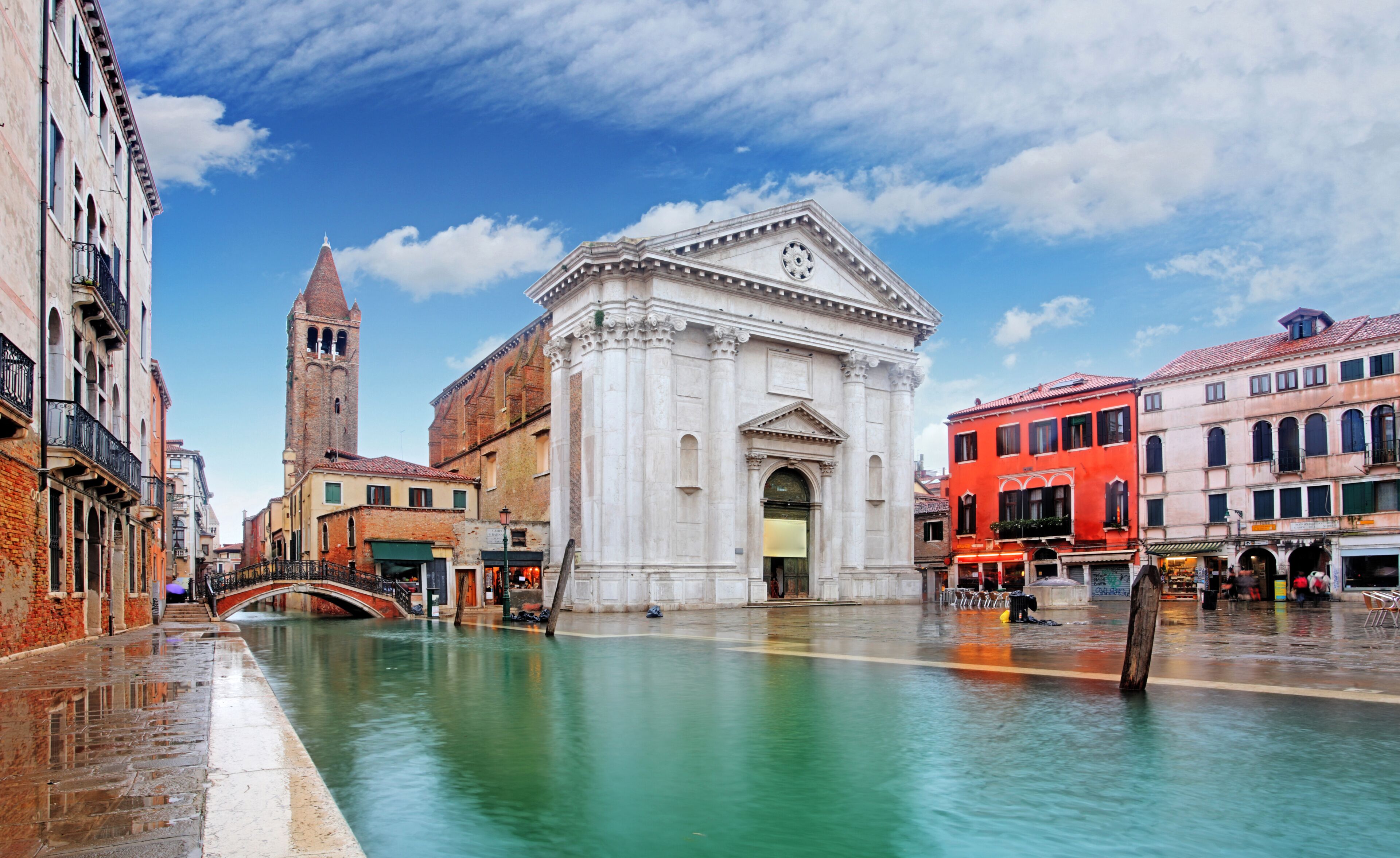 Um canal em Veneza com edifícios históricos, um campanário e um prédio vermelho.