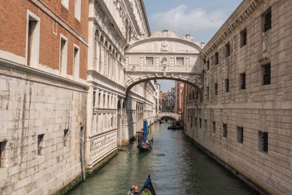 A narrow canal flanked by historic buildings, a bridge, and a gondola with a passenger.