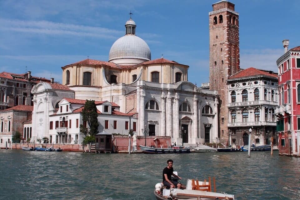 A boat on a canal with historic buildings and a tall tower in the background.