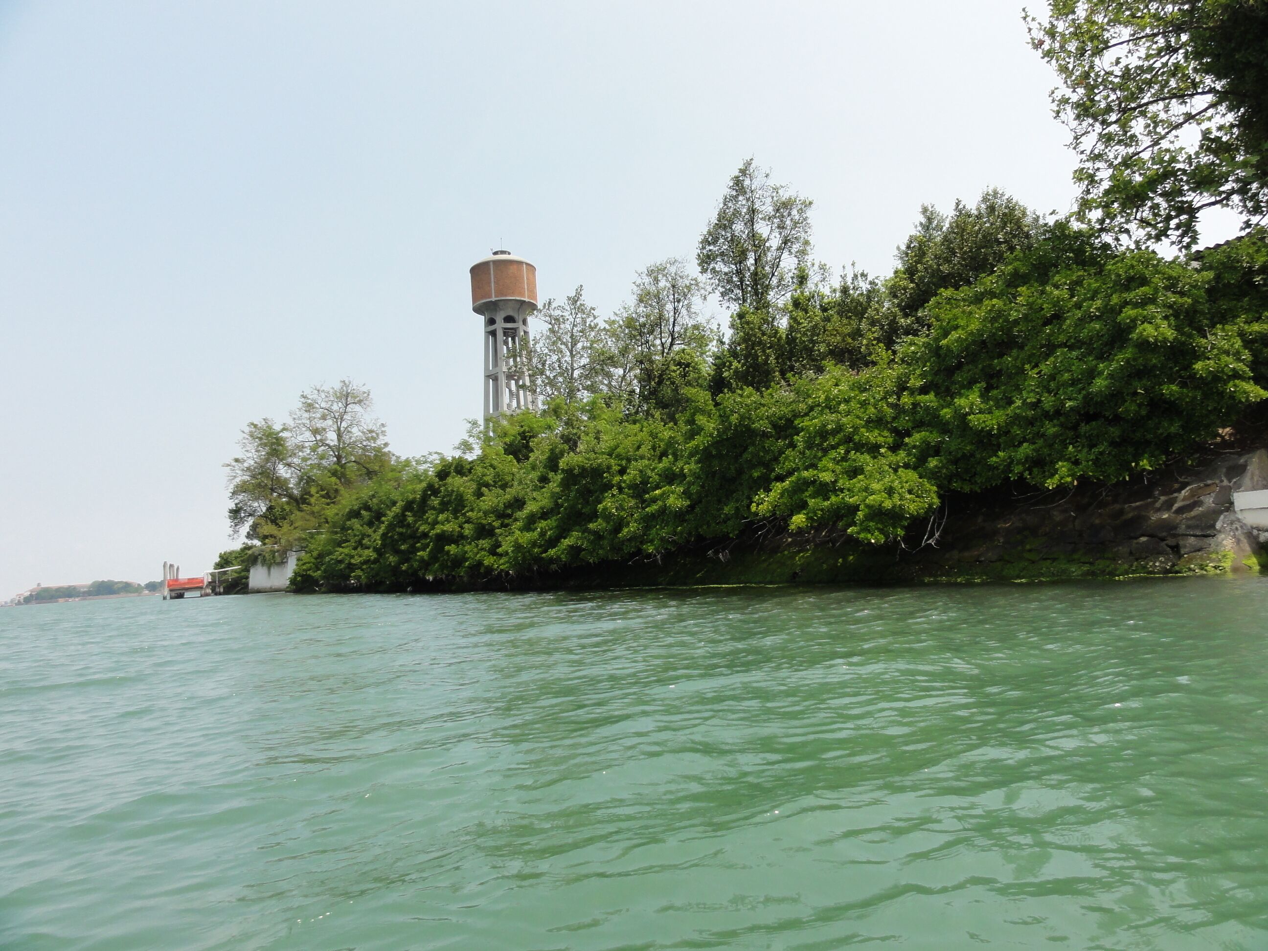 A water tower, dense green foliage, and a calm river.