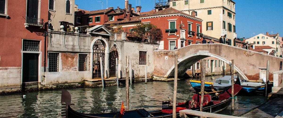 A canal with a gondola docked at a bridge, surrounded by historic buildings.