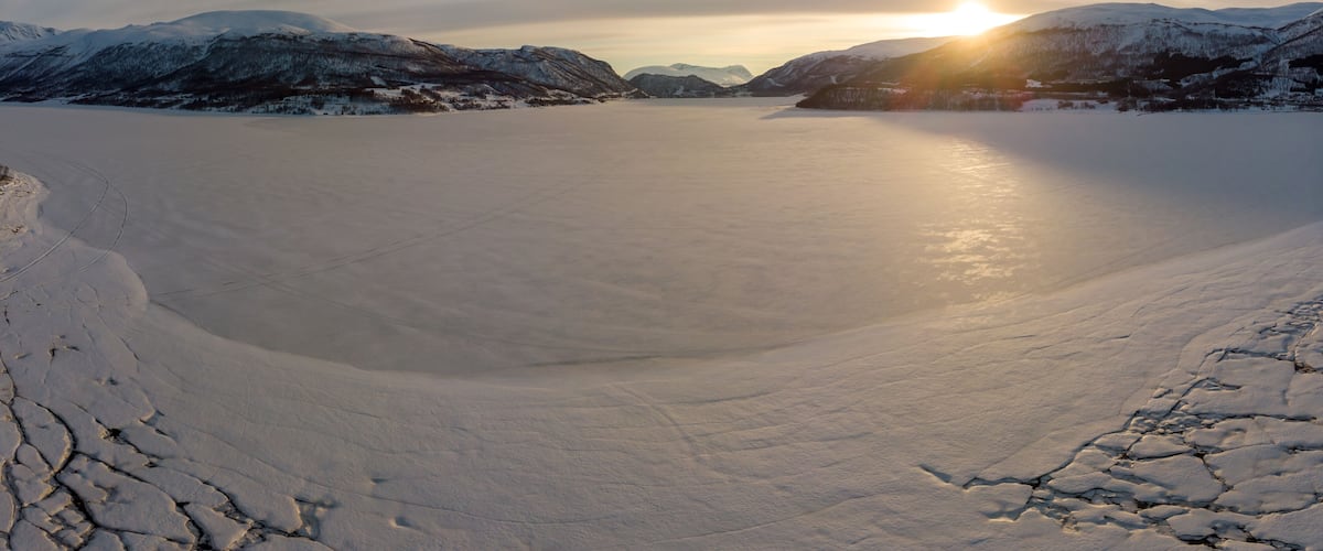 A frozen lake surrounded by snow-covered mountains during sunset.