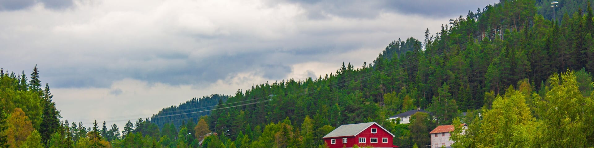 A river flowing through a forested valley with red buildings and a bridge.