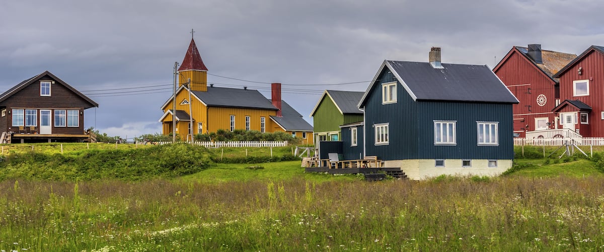 A coastal village with colorful houses, a church, and a grassy field.