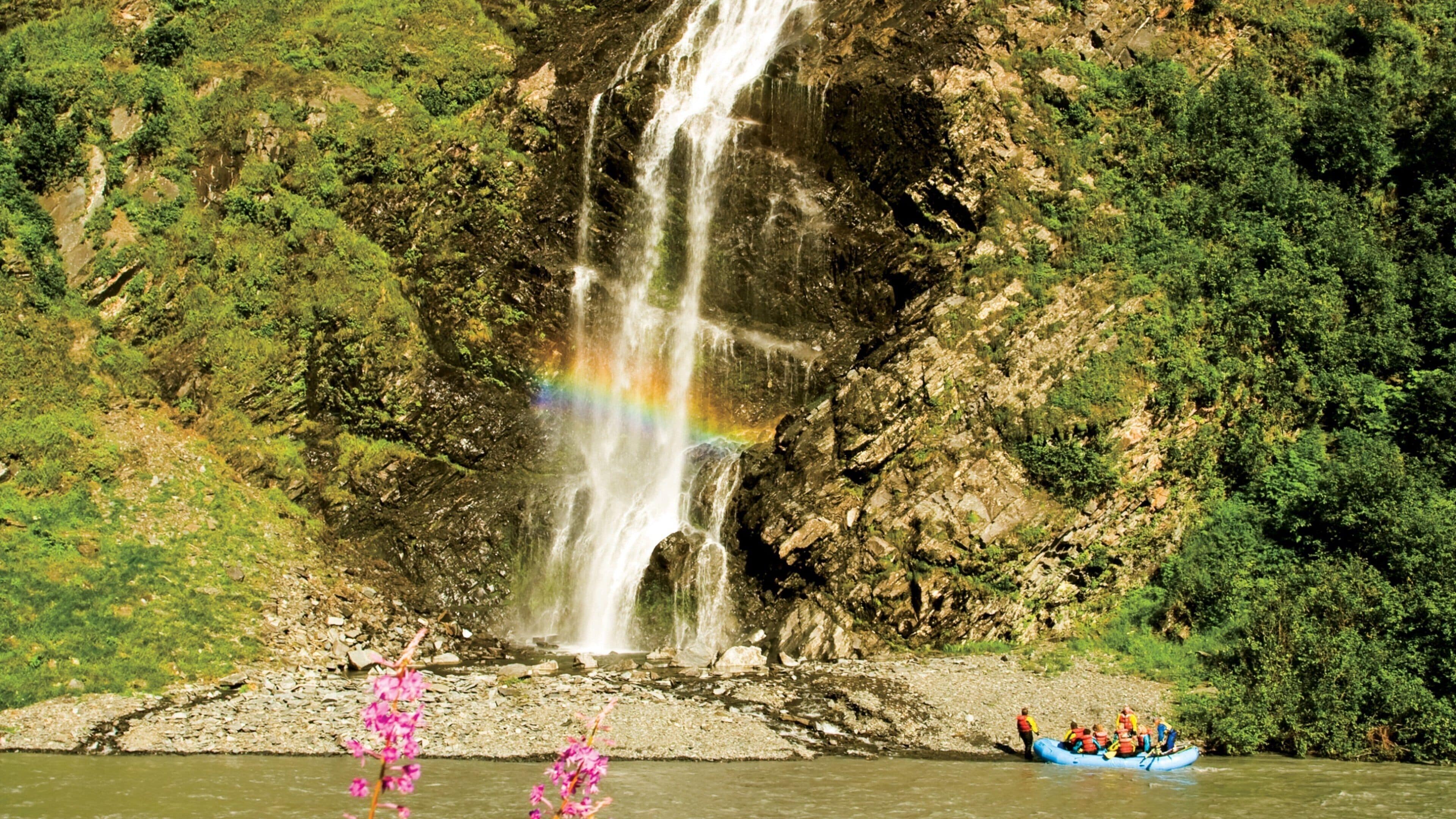 A waterfall with a rainbow, surrounded by lush greenery.