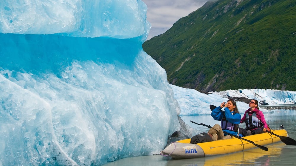A glacier with a yellow inflatable raft and two people paddling.