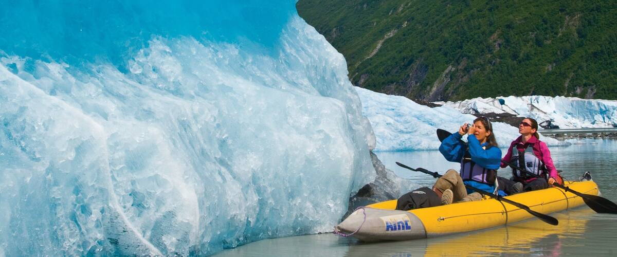 A glacier with a yellow inflatable raft and two people paddling.