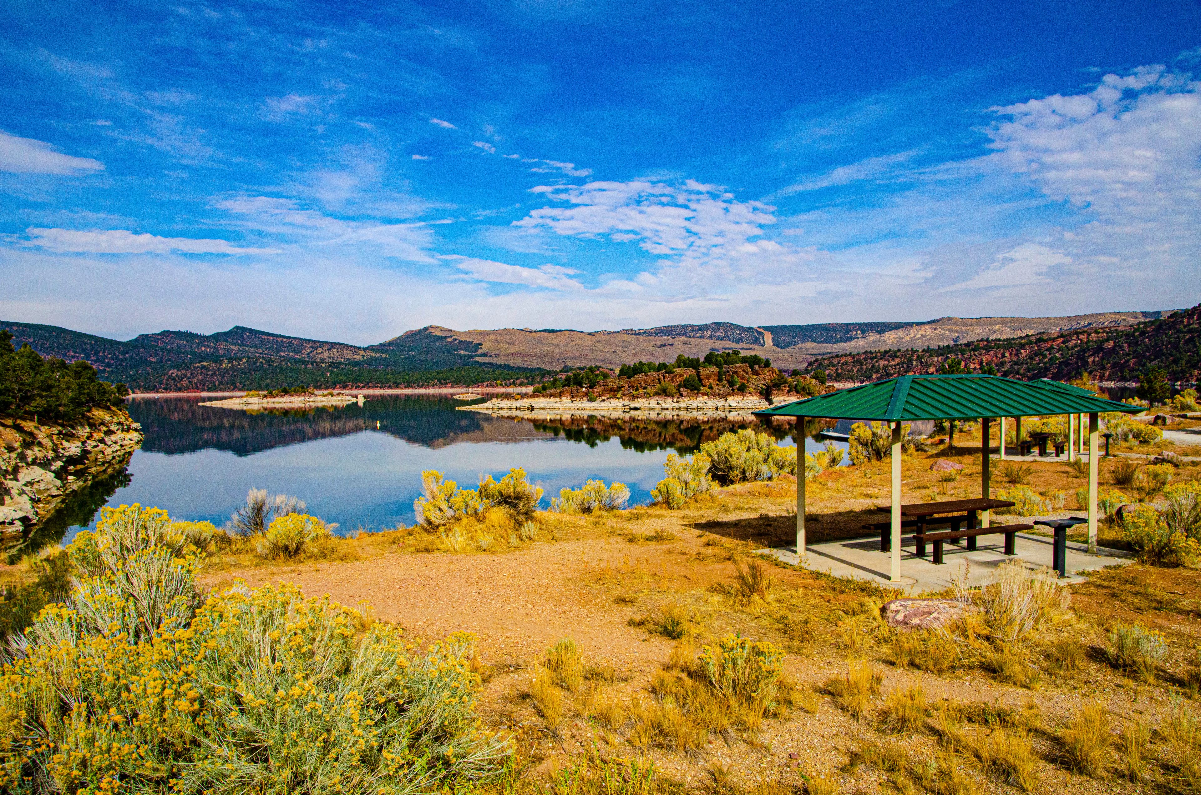 A serene lakeside scene with a green gazebo, a clear sky, and surrounding hills.