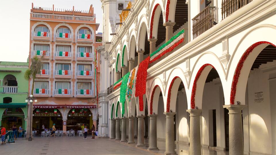 A plaza with a restaurant, a building with balconies decorated with Mexican flags, and arches adorned with red tinsel.