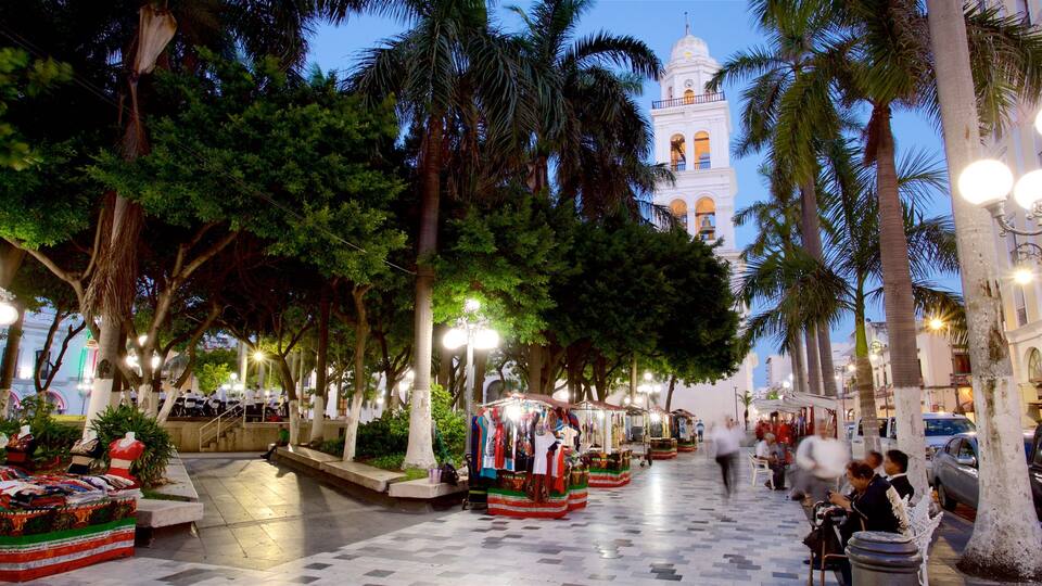 A bustling street with palm trees, a market stall, and a white building with a bell tower in the background.