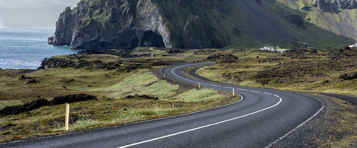 A winding road curving around a green mountain with a steep cliff face.