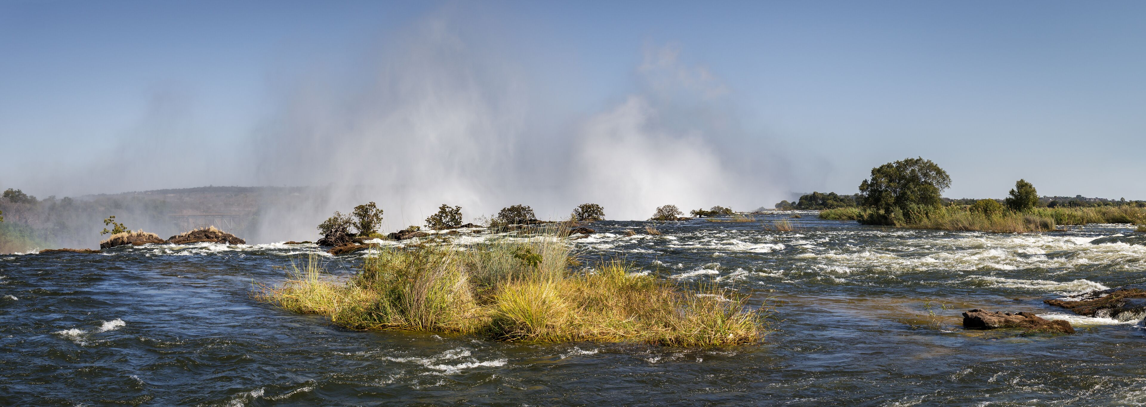 A river with rapids, a waterfall, and surrounding vegetation.