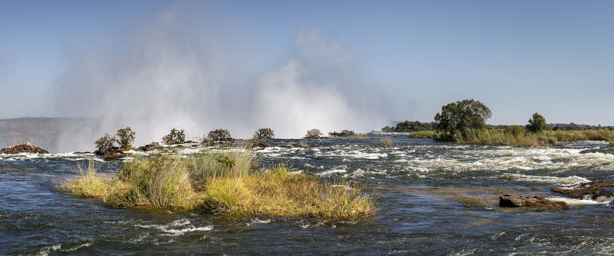 A river with rapids, a waterfall, and surrounding vegetation.