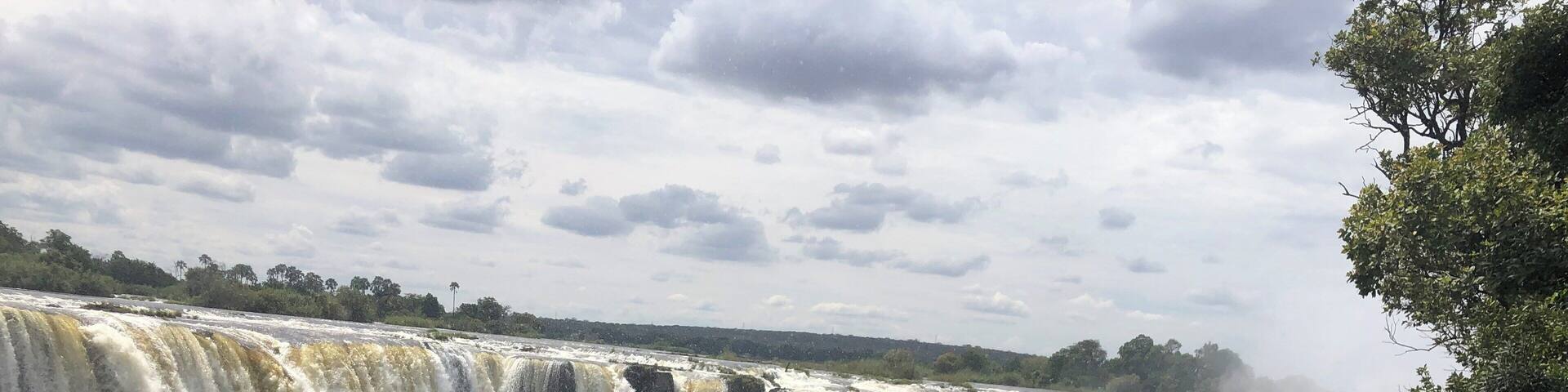 A large waterfall with multiple tiers, surrounded by lush greenery and a cloudy sky.
