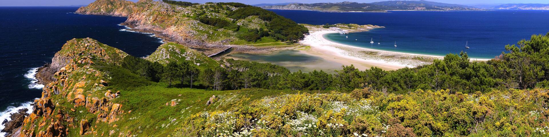 A coastal landscape with a beach, a rocky outcrop, and a clear blue sky.