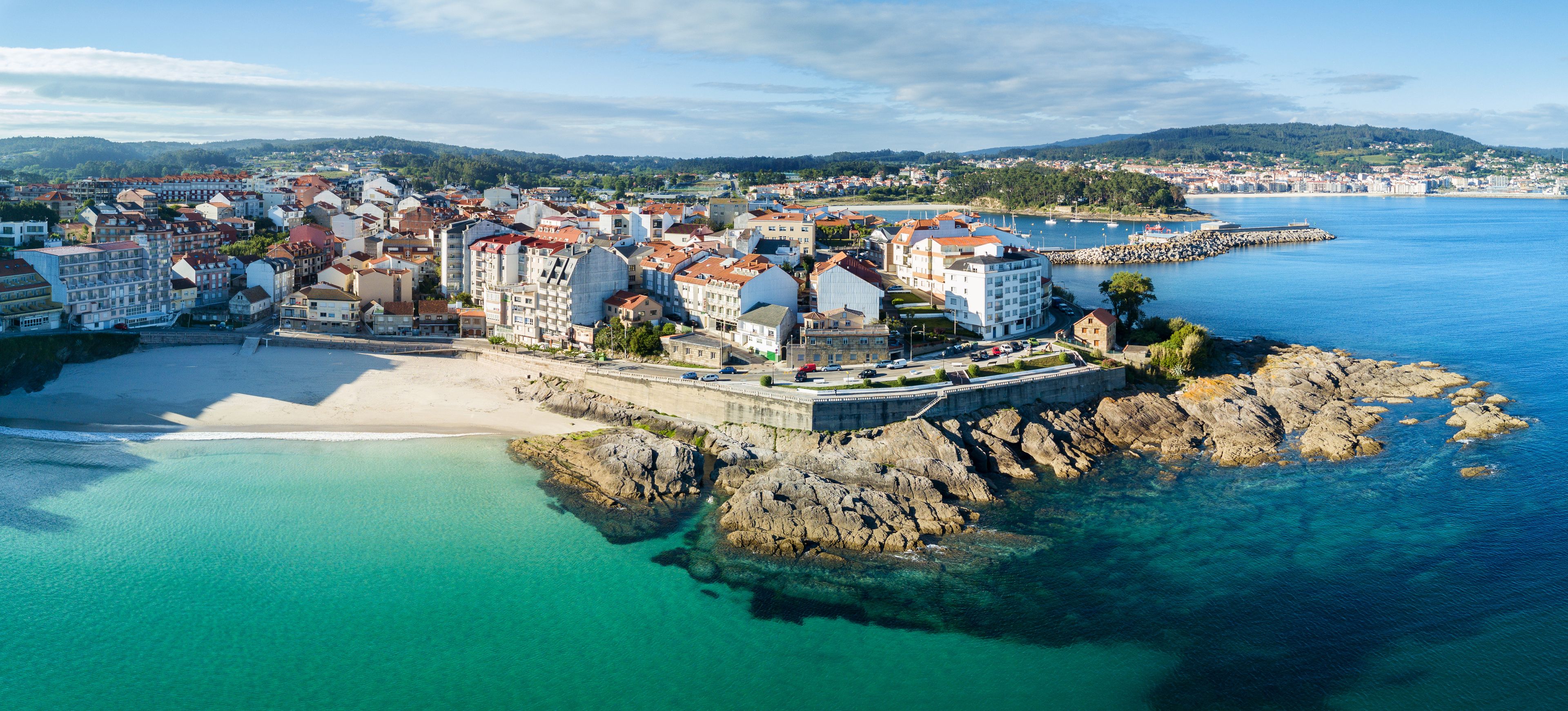 A coastal town with buildings, a beach, and rocky outcrops.