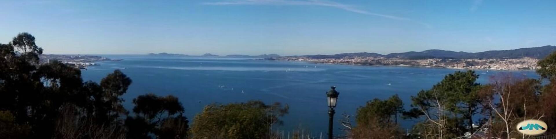 A coastal cityscape with a clear view of the ocean, a lighthouse, and distant hills.