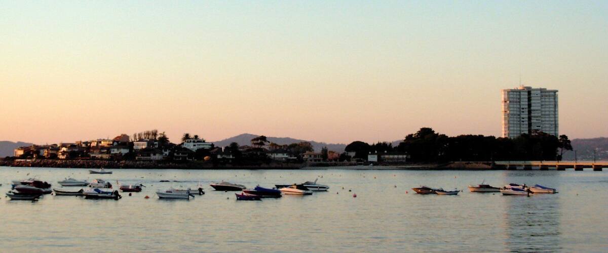 A coastal cityscape with boats docked in the water and a tall building in the background.