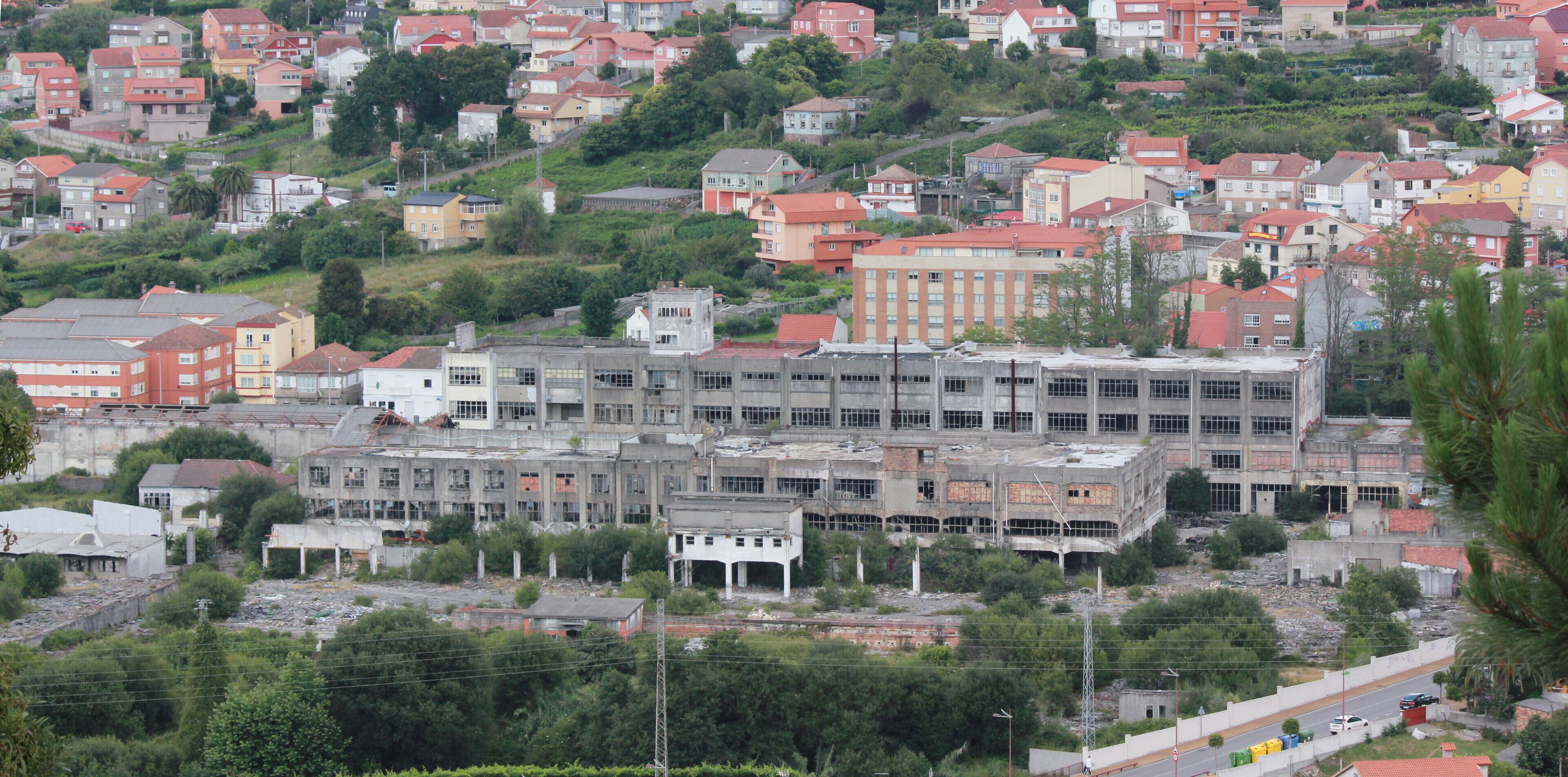 A hillside residential area with various buildings, including a large, unfinished structure in the foreground.
