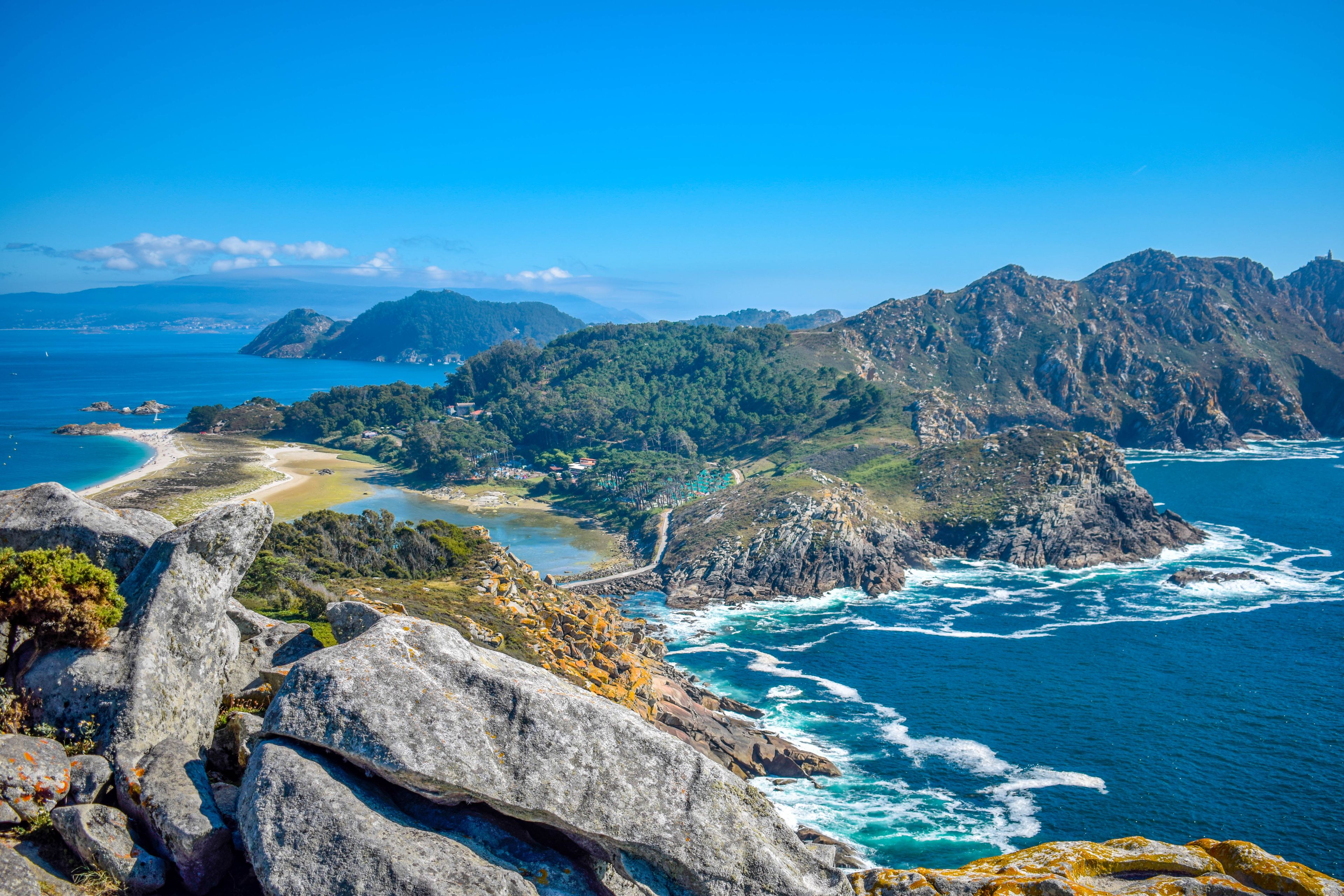 A coastal landscape with rocky cliffs, a beach, and a clear blue sea.