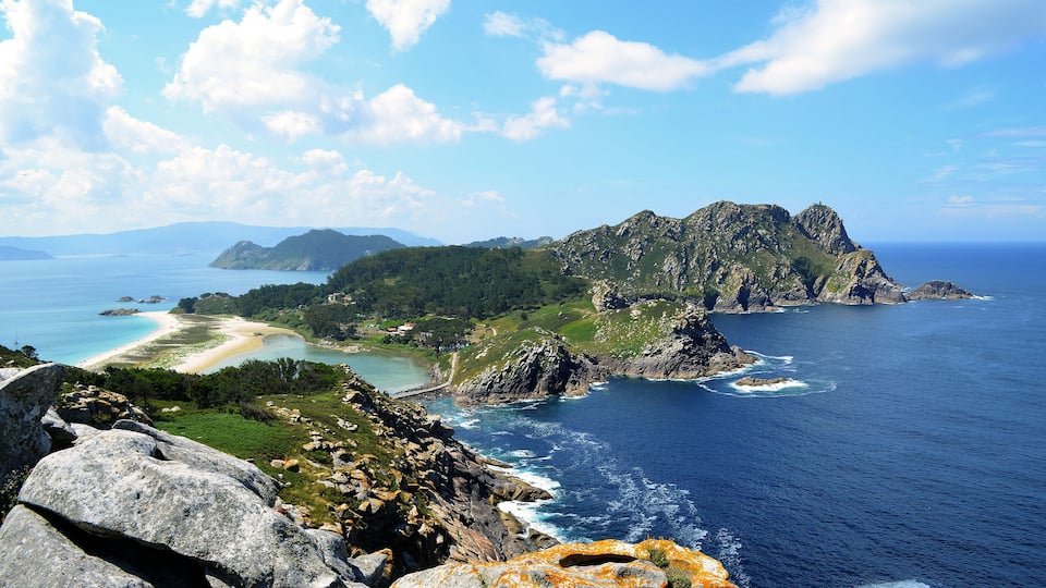 A coastal landscape with rocky cliffs, a beach, and a clear blue sea.