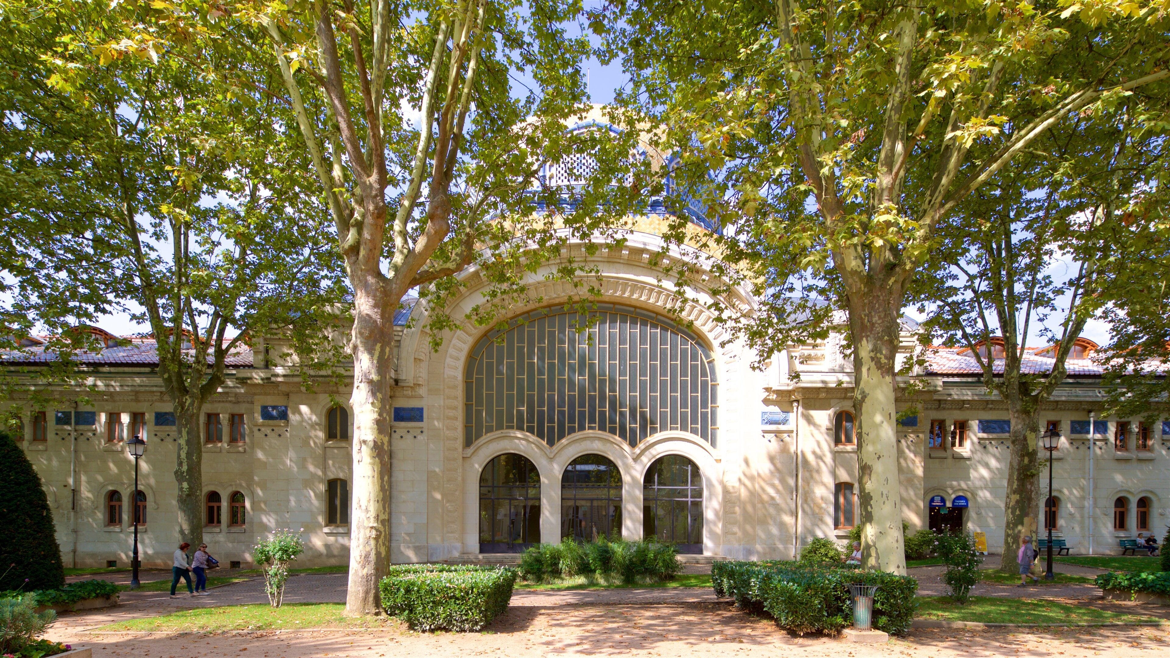A historic building with a large arched window and columns, surrounded by trees and a well-maintained garden.