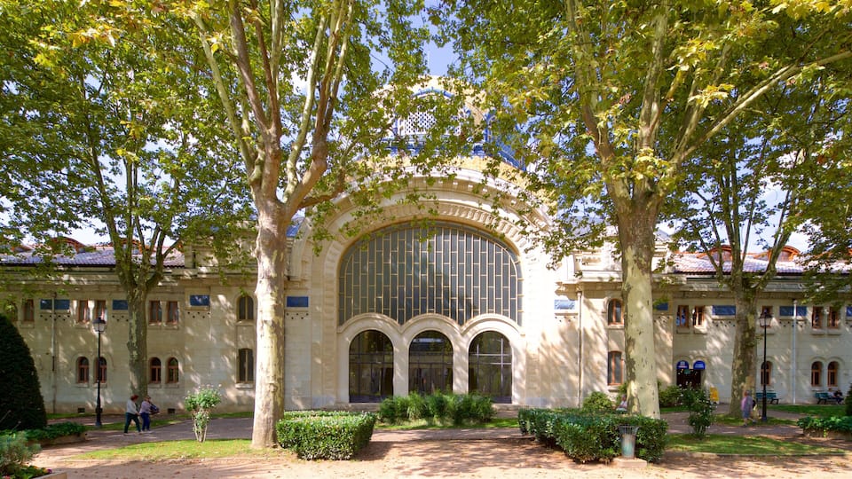 A historic building with a large arched window and columns, surrounded by trees and a well-maintained garden.