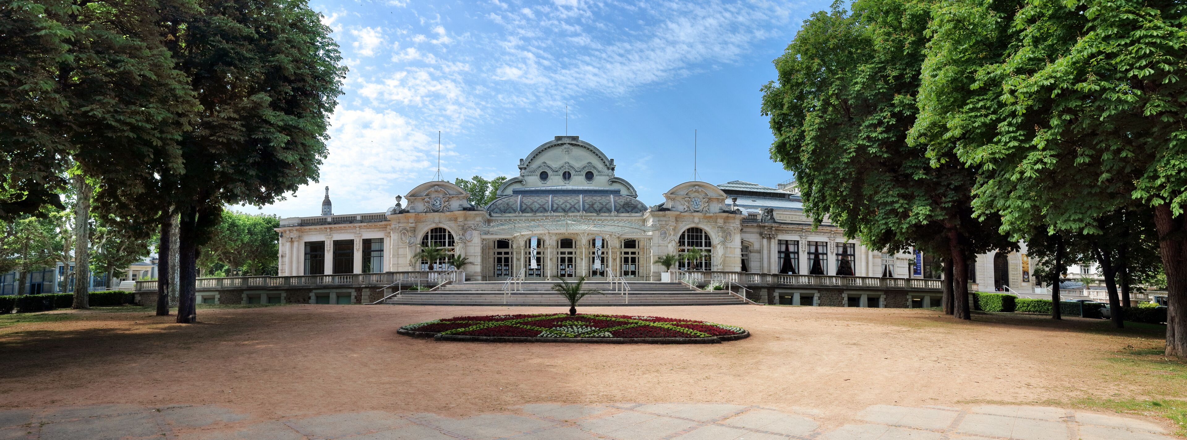 Un edificio histórico con una cúpula y un campanario, rodeado de árboles y un patio empedrado.