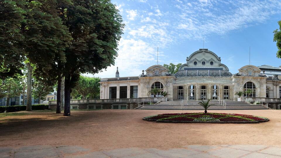 Un edificio histórico con una cúpula y un campanario, rodeado de árboles y un patio empedrado.
