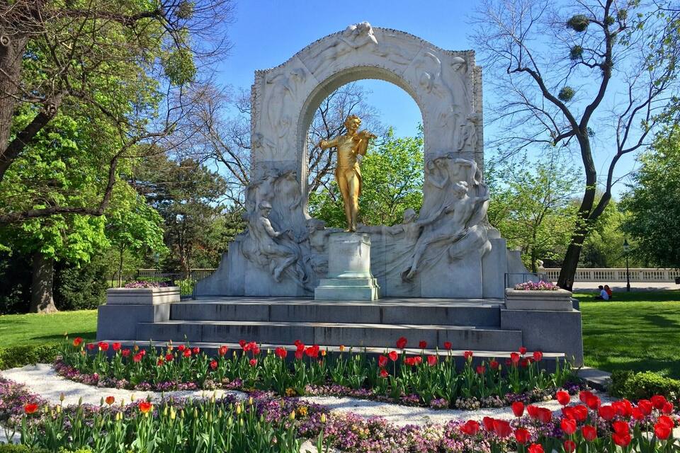 Estátua de mulher num parque com tulipas vermelhas e árvores.
