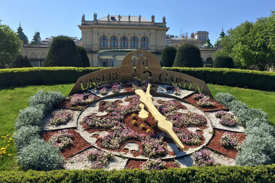 A garden with a large sundial and a building in the background.