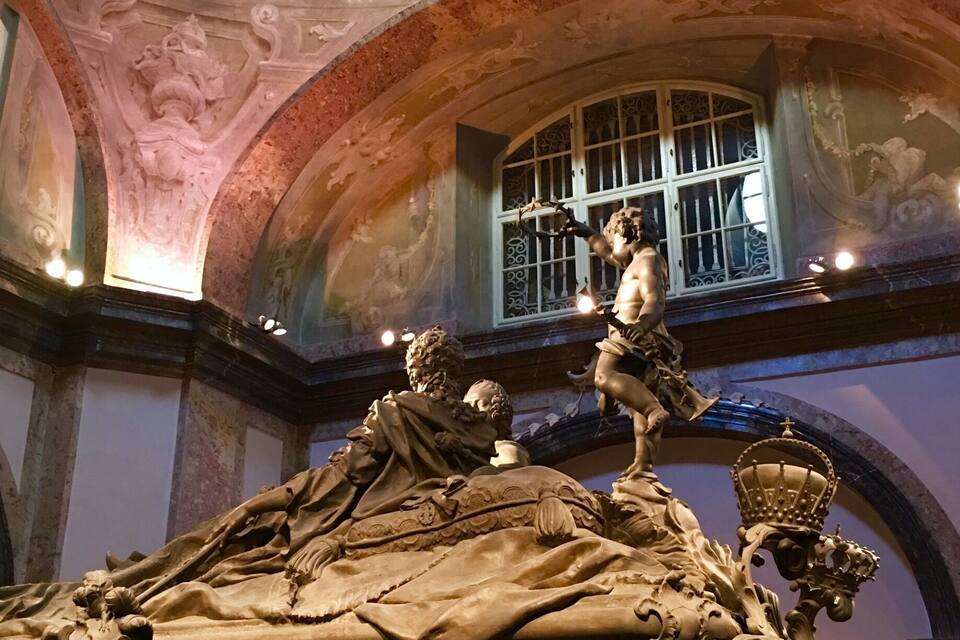 Escultura detallada d'una figura reclinada amb una corona, envoltada d'altres figures i un lleó.