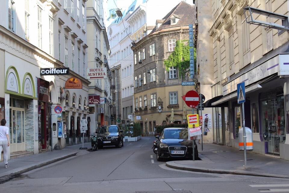 Calle con edificios, un letrero que dice 'Hotel Austria' y coches estacionados.
