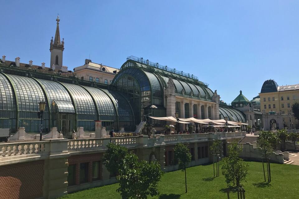 A large glass greenhouse structure with a dome roof, surrounded by a well-maintained lawn and a few trees.