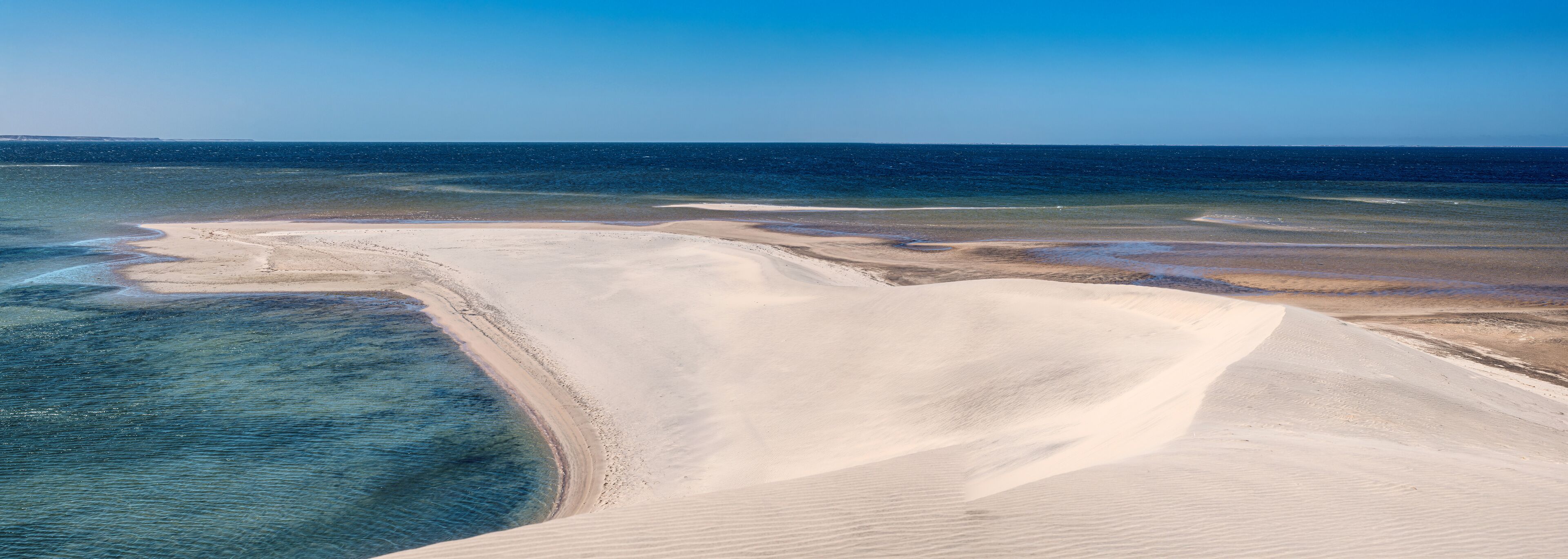 A coastal landscape with sand dunes and a clear blue sea.
