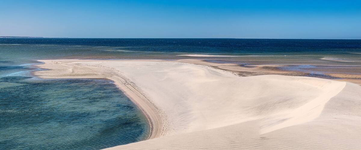 A coastal landscape with sand dunes and a clear blue sea.