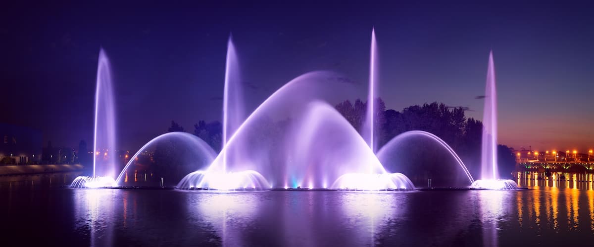 A nighttime fountain display with multiple water jets illuminated in purple.