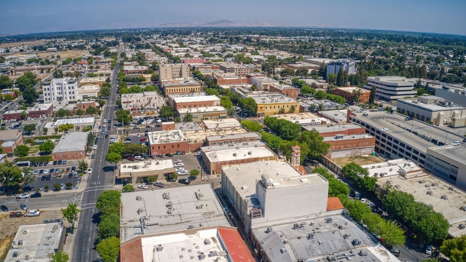 An aerial view of a city with a mix of historic and modern buildings, a prominent road, and a distant mountain range.
