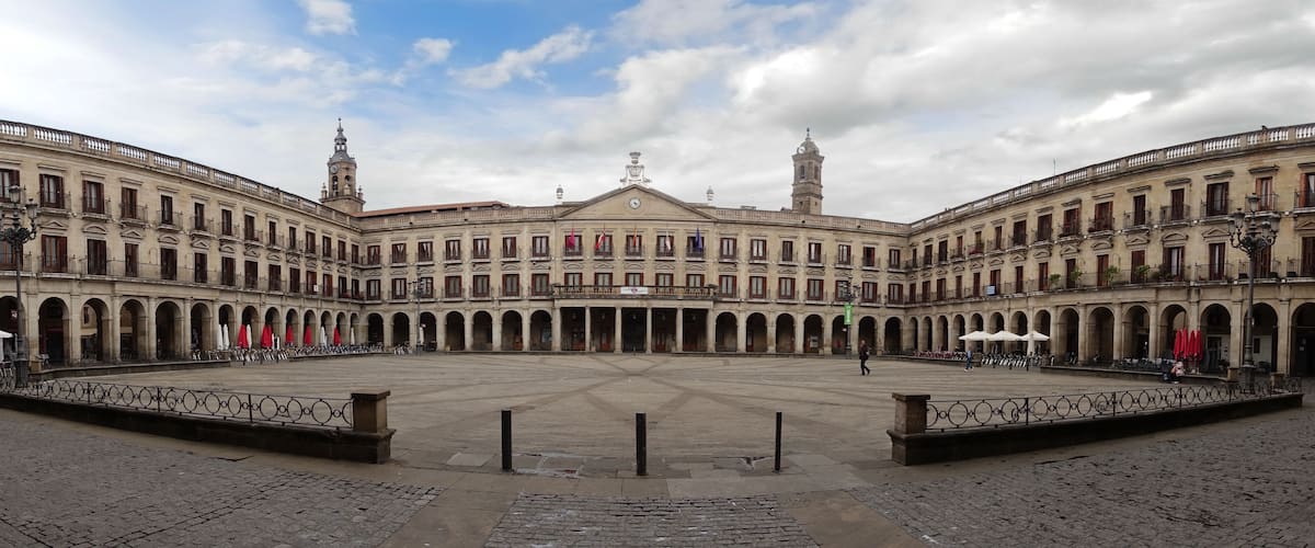 A historic courtyard with a central open space, surrounded by buildings with balconies and a clock tower.
