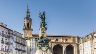 A historic square with a clock tower, a statue, and classic European architecture.