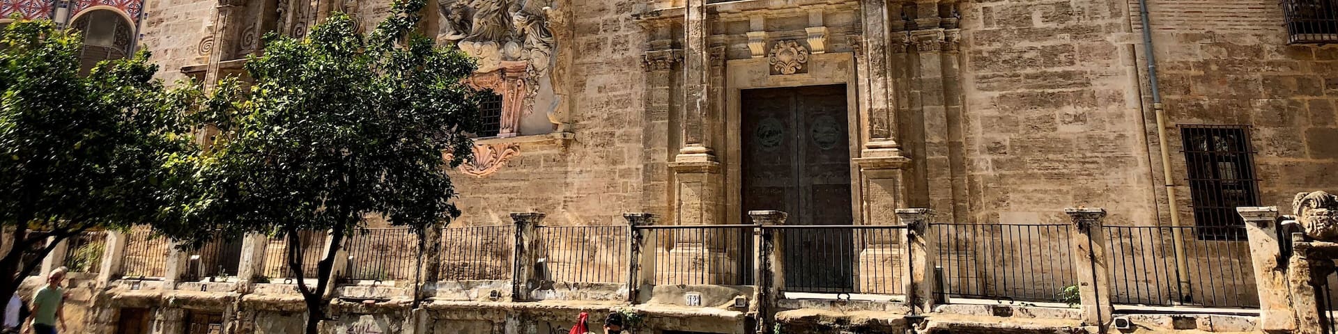 The primitive church of Sant Joan Mercat was erected in the suburb of the city known as the Boatella. From its old Gothic structure there is still the nave and the large blind oculus, known as "La O de Sant Joan", which was conceived as a large rosette on the façade of the feet.
In 1592 the church suffered a spectacular fire that forced an almost total reconstruction throughout the seventeenth and eighteenth centuries. It stands out for the infrequent the wide façade of the Market, conceived as a grandiose stone altarpiece on a terrace that dominates the square in front of the Lonja, forming a unique urban set.
It is presided by the sculpture of the Virgin of the Rosary, work in stucco by Jacopo Bertesi, and on it stands the clock tower, flanked by the two Santos Juanes and crowned by the famous "Pardal de Sant Joan", the weather vane to which -according to tradition- was made to look at the children when their humble parents abandoned them in the square. In the lower part of the terrace there are "les covetes de Sant Joan", semi-basements in which once were junkyards and old shops, part of the living history of Valencia.
The interior of the temple is an overflowing Baroque imagination, with statues of Bertesi representing characters of the Twelve Tribes of Israel, and especially the set of frescoes that Antonio Palomino executed in the vault.