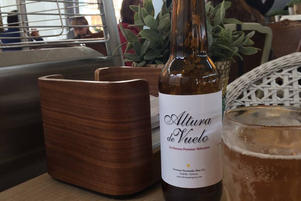 A bottle of Altura de Viedo beer, a glass of beer, and wooden coasters on a table.