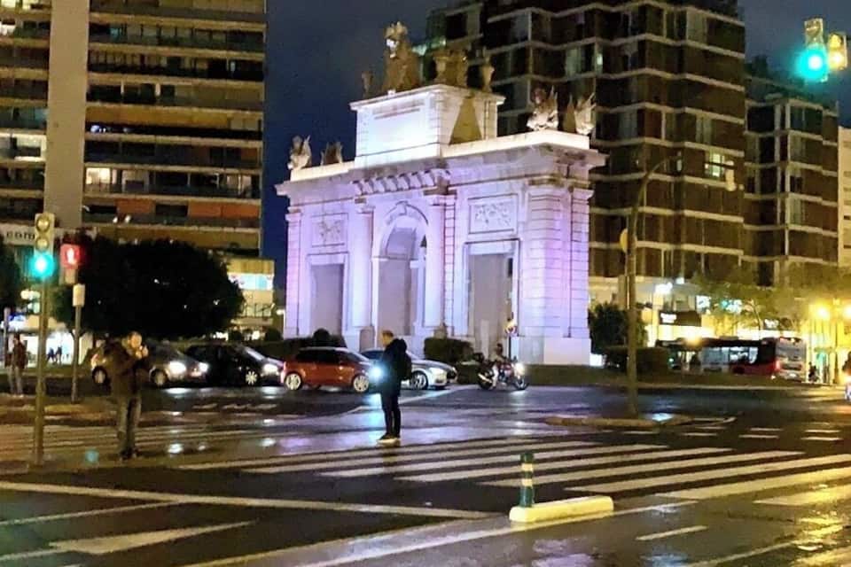 Une vue nocturne d’une ville, avec un bâtiment illuminé qui se distingue par son architecture classique et ses statues.